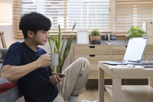 穿着便装的年轻人坐在客厅里用笔记本电脑上网。图片下载