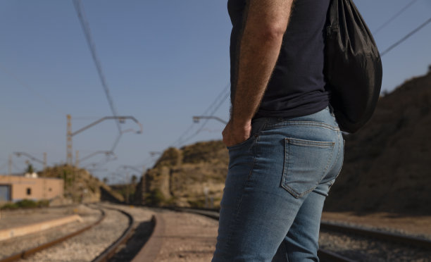 侧视图的成年男子在牛仔裤提着包等待在铁路月台图片下载