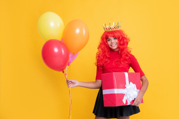 微笑的青少年儿童在皇冠与礼物盒和黄色背景的派对气球图片下载