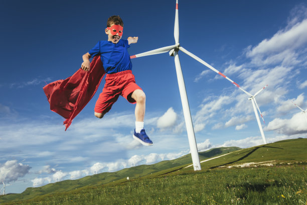 超级英雄小孩在风力发电场前面。小孩子玩超级英雄。图片下载