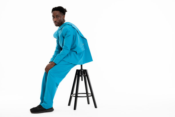 全身照片，深色皮肤的模特男子年轻穿着蓝色休闲西装，看着相机的视角，一边坐在黑色椅子上，戴着滑稽的发型图片下载