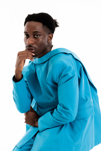 照片中深思熟虑的非裔美国人手握靠近下巴的手臂，看着镜头，严肃的心情，穿着休闲的蓝色西装，滑稽的发型图片下载