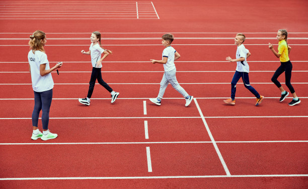 训练运动员的女教练员。一群孩子在体育场的跑步机上跑步。体育的概念，成就，学习，目标，技能。小男孩和女孩在户外训练。图片下载