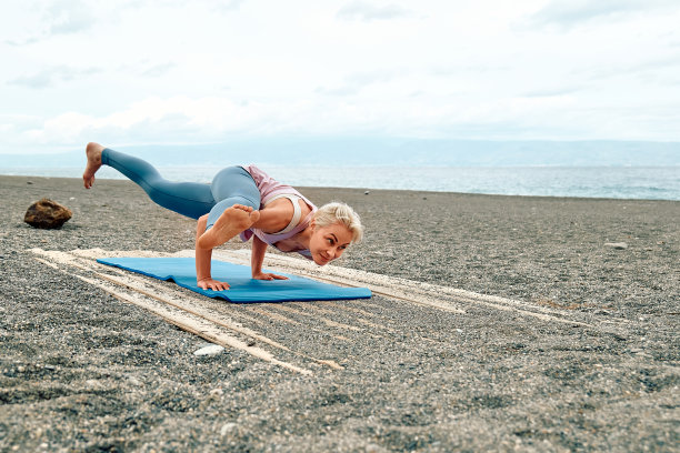 苗条的女人做maksikanagana或蜻蜓姿势在海滩上早上。增强腿部肌肉和身体协调性。在户外练习瑜伽图片下载