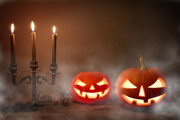 鬼魅的万圣节南瓜，杰克灯，有着邪恶的脸和眼睛，黑暗背景上有雾的旧蜡烛。图片下载