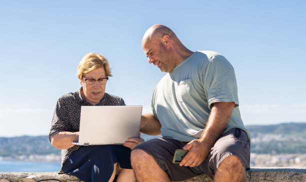 中年男子坐在户外，帮助年长妇女使用笔记本电脑图片下载