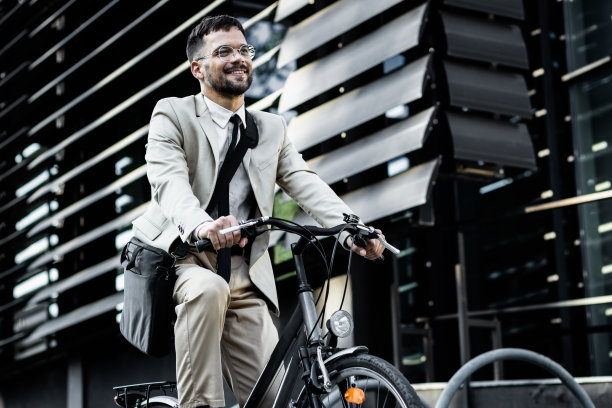 商人在现代化的办公楼前骑自行车。图片下载