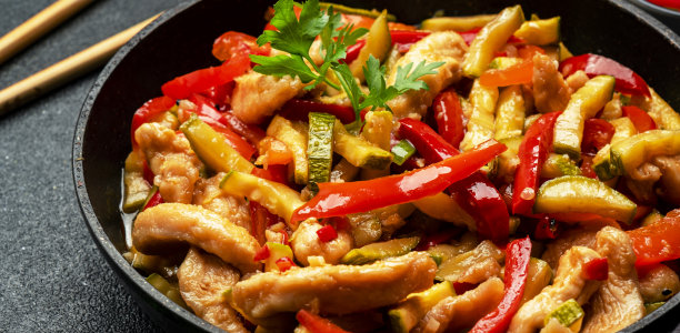 亚洲菜，加入鸡肉，红辣椒粉和西葫芦在煎锅里翻炒。黑色厨房餐桌背景，俯视图，特写图片下载