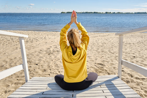 在海边上瑜伽课的时候，穿着运动服的妇女坐在莲花的位置上冥想。练习瑜伽，呼吸，冥想，做莲花形练习。健康的概念图片下载