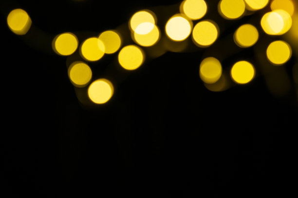 金色迷离的灯光在黑色背景上散焦，作为节日的背景图片下载