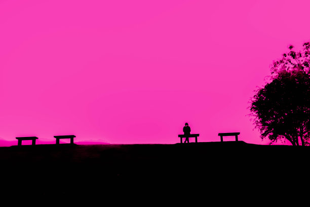 女人坐在小山上的长凳上，颜色效果与剪影暗调和粉色背景图片下载