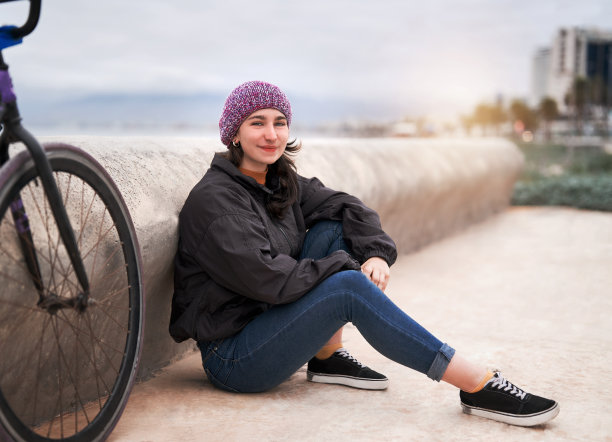 年轻的拉丁女子骑自行车画像坐在路边一辆自行车旁高兴图片下载