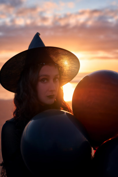 拉丁妇女穿着黑色，戴着女巫帽和气球在日落肖像图片下载