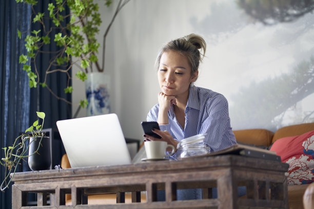 成熟的亚洲女性在家使用笔记本电脑和手机工作图片下载