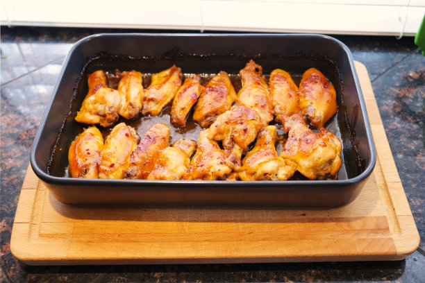 新鲜出炉的鸡翅在烤盘煎锅上的木砧板在厨房桌子柜台表面接近顶部查看食物照片。自制烤炉烤家禽。在家做饭图片下载
