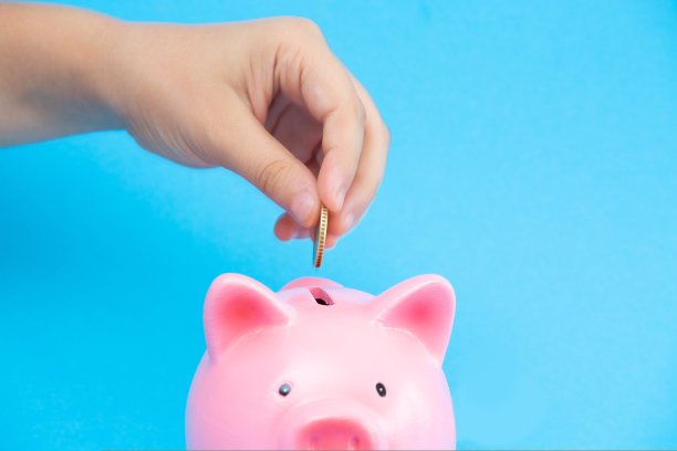 孩子们的手把一枚硬币放在蓝色背景的粉色储蓄罐里。对孩子未来投资的概念，储蓄，理财规划图片下载
