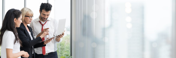 商务团队的男男女女在笔记本电脑上讨论工作，并使用贴在玻璃墙上的笔记。一群公司不同的同事在办公室进行头脑风暴和规划业务战略图片下载