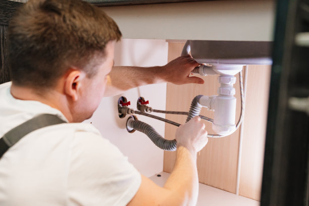 一名男水管工正在修理浴室水槽下的虹吸。图片下载