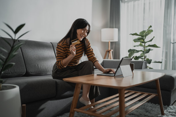 亚洲女性开心地笑着拿着信用卡，用电子平板电脑在网上购物。图片下载