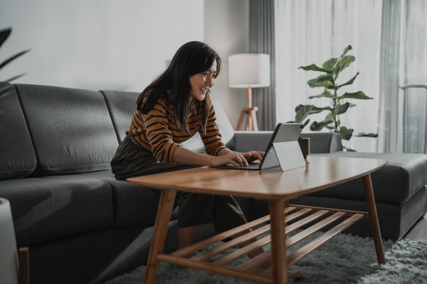亚洲妇女开心地微笑着在平板电脑键盘上打字，在家里的客厅里工作、学习或浏览社交媒体。图片下载
