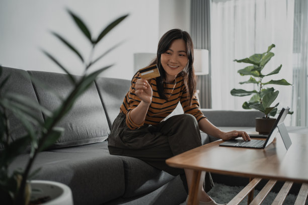 亚洲女性开心地笑着拿着信用卡，用电子平板电脑在网上购物。图片下载