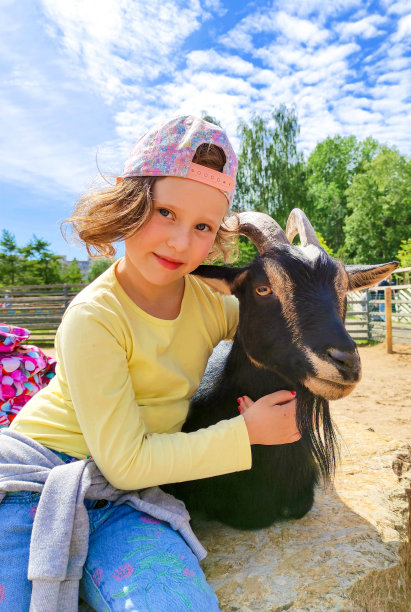 一个7岁的白人女孩，微笑着看着镜头，抱着一只黑色的山羊。图片下载