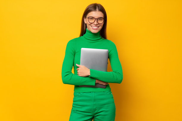 微笑的女学生肖像在绿色拿着笔记本电脑，孤立在黄色背景图片下载