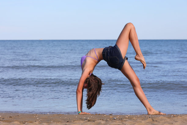 年轻苗条的女孩穿着短牛仔裤短裤在海边做体操图片下载