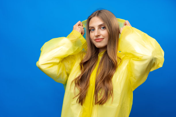 年轻的金发女人穿着黄色雨衣微笑的镜头在蓝色的背景在工作室图片下载
