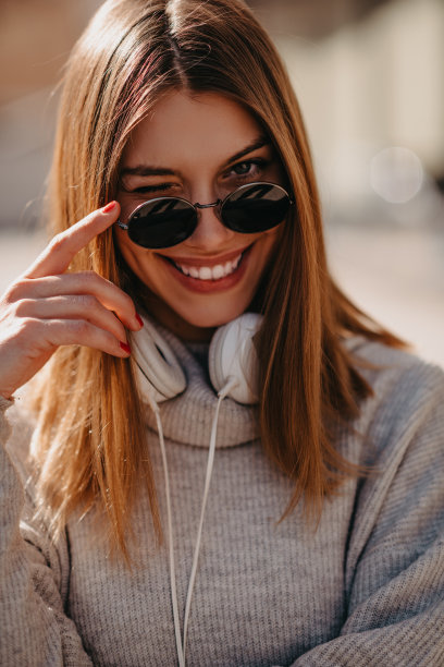 一个现代女孩戴着墨镜走在街上，戴着耳机听着音乐。图片下载