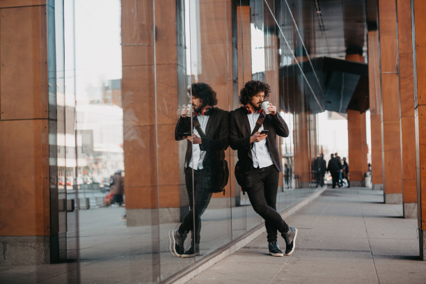 时髦的商人带着皮制公文包在金融区用智能手机听着音频歌曲，戴着耳机喝着咖啡图片下载