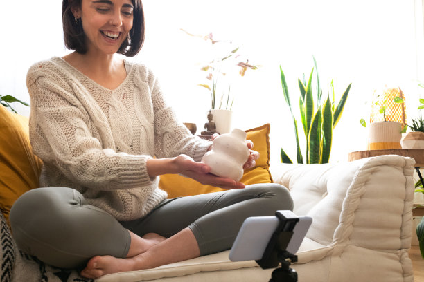 快乐的年轻白人女性DIY影响者用智能手机记录视频显示手工陶瓷花瓶。副本的空间。图片下载