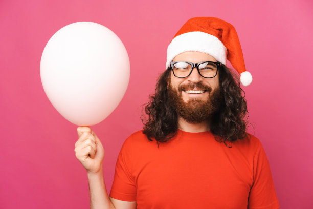 一个男人戴着圣诞帽，拿着一个白色气球的特写照片。图片下载