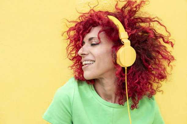 一个微笑的拉丁妇女的肖像，红色的爆炸头，穿着t恤，听音乐与黄色的耳机在黄色的背景图片下载