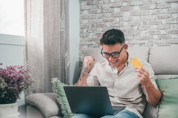 一个年轻人用笔记本电脑在网上商店购物。快乐的男孩用信用卡在网上购物图片下载