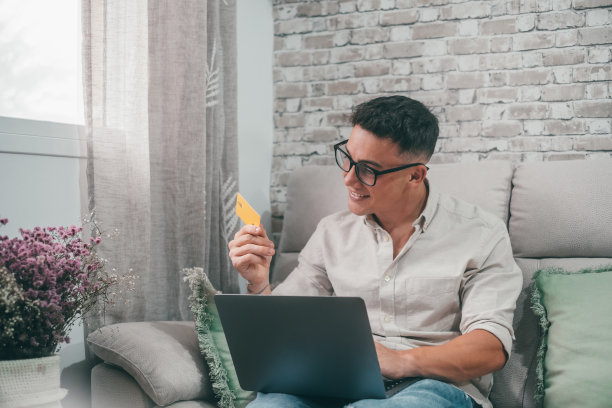 一个年轻人用笔记本电脑在网上商店购物。快乐的男孩用信用卡在网上购物图片下载