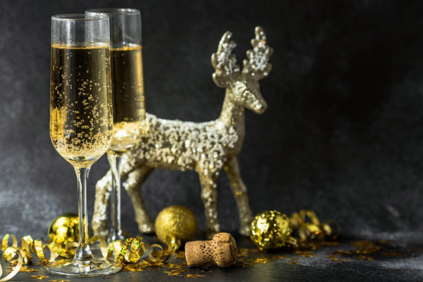 2023年新年快乐。圣诞节和新年假期背景与复制空间。两杯和驯鹿香槟与闪烁的灯光在黑暗的背景。图片下载