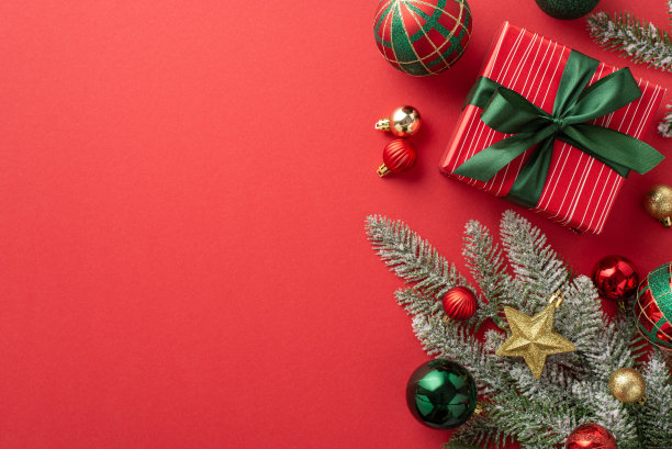 圣诞节的概念。顶视图照片松枝在霜冻装饰星星装饰金绿红色小饰物和礼品盒缎带蝴蝶结孤立的红色背景与空白图片下载