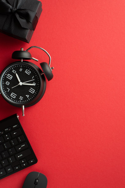 黑色星期五的销售概念。顶视图垂直照片黑色闹钟礼盒丝带蝴蝶结电脑鼠标和键盘上孤立的红色背景图片下载
