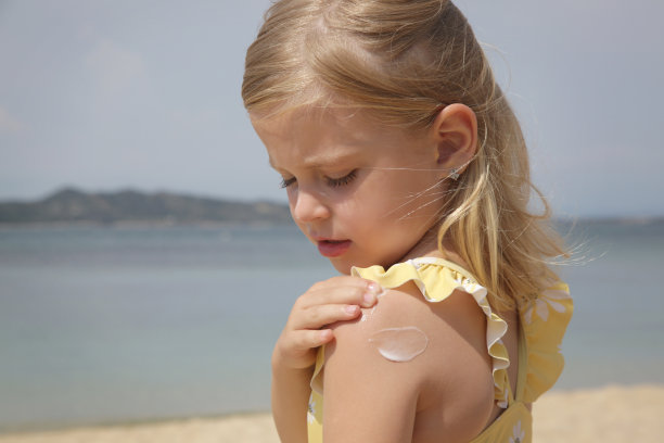 可爱的小女孩在海滩上涂防晒霜。暑假期间为宝宝防晒的防晒乳液。旅行期间儿童皮肤护理。图片下载