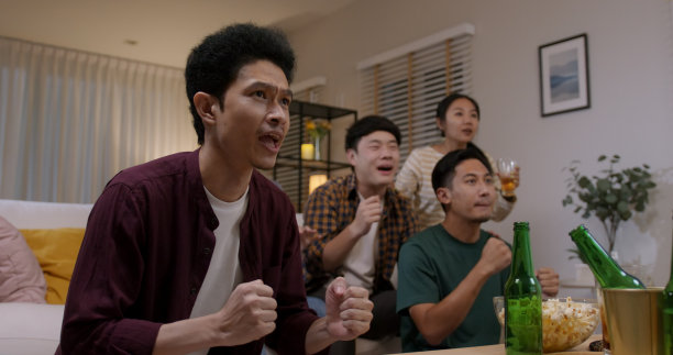 一群年轻的成年朋友男女亚洲人坐在沙发沙发欢乐的派对有趣的游戏FIFA世界杯直播电视在家里唱着歌手举着牌子跳着疯开心赢欢腾的脸。图片下载
