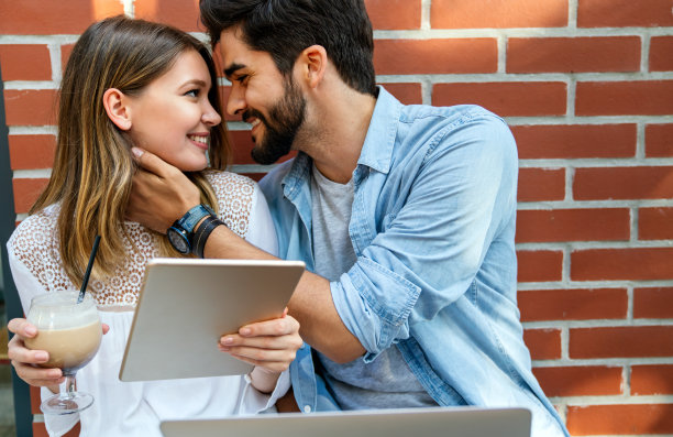 一对情侣坐在咖啡馆里微笑，用笔记本电脑，享受时光，喝咖啡。图片下载