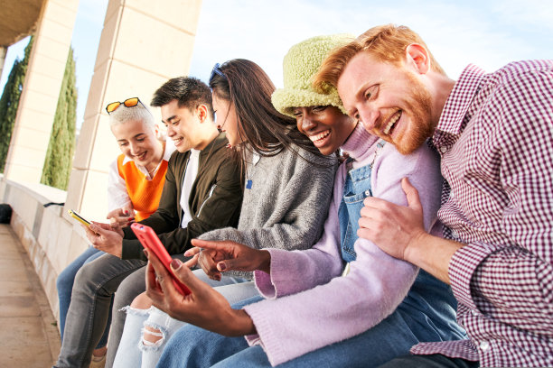 一群多种族的朋友一起在户外使用手机玩智能手机。多元化的人见面，放松的连接，沟通的社区概念。图片下载