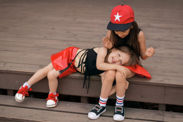 一个有趣的笑着的小女孩躺在她姐姐的腿上。时髦的孩子们穿着红黑相间的摇滚时装图片下载