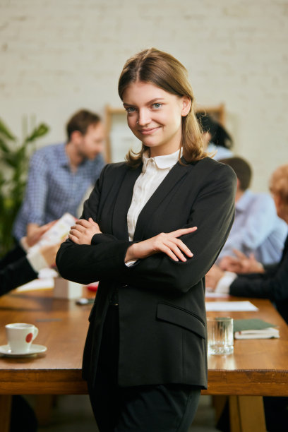 年轻而成功的商业女性的肖像。在现代化的办公室里和同事开会时，快乐聪明的女孩穿着商务套装图片下载