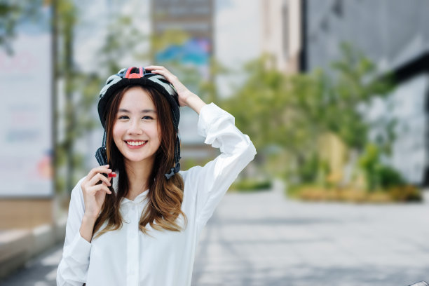 年轻的亚洲女商人戴着头盔，骑着自行车站在城市街道上看手机。图片下载