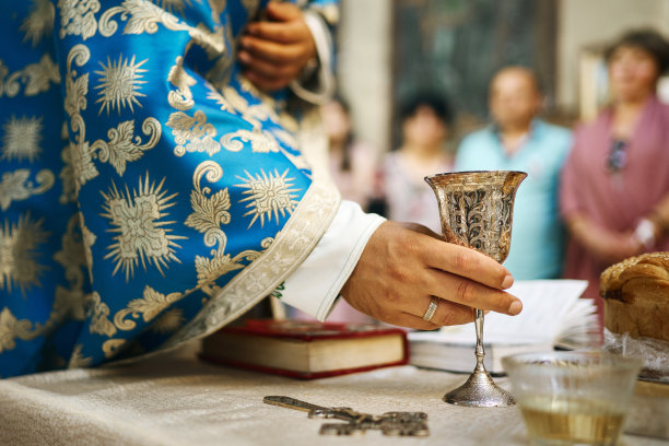 在东正教教堂举行的婚礼仪式上，牧师的手和盛有酒的仪式婚礼杯图片下载