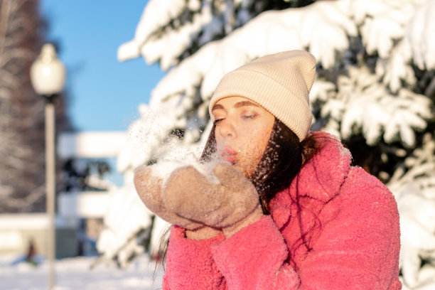 年轻漂亮的女人正在吹掉手上的雪。冬天，圣诞节和新年快乐的概念。图片下载