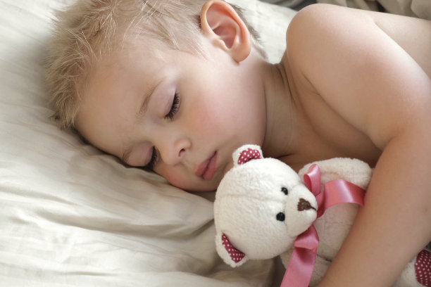 睡在床上的孩子。可爱的小孩在白色毯子上甜甜地睡觉。2岁的小孩和泰迪熊玩具一起睡觉。脸特写。小男孩白天躺在枕头上睡觉。4K图片下载