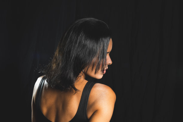 工作室肖像的年轻女子在黑色t恤对纯黑色的工作室背景。图片下载